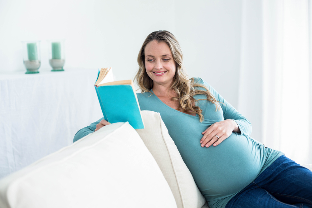Pregnant woman reading a book on the couch Pregnant woman reading a book on the couch